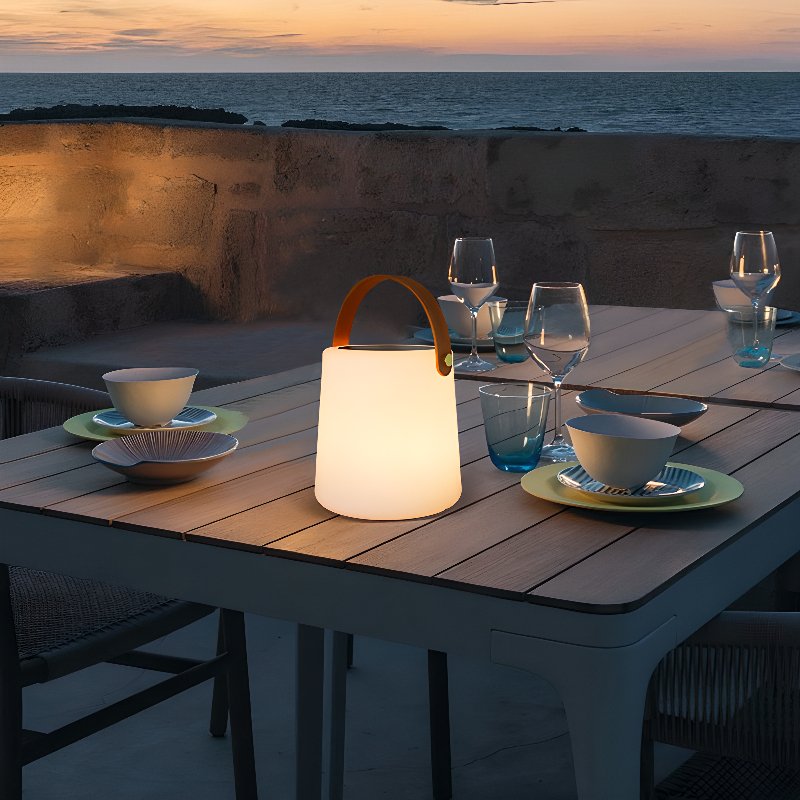 The lamp lit on a laid table on a stone terrace above the sea at dusk