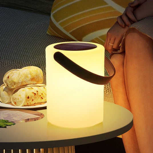 The lamp lit on a terrace table beside a plate of bread and a seated guest