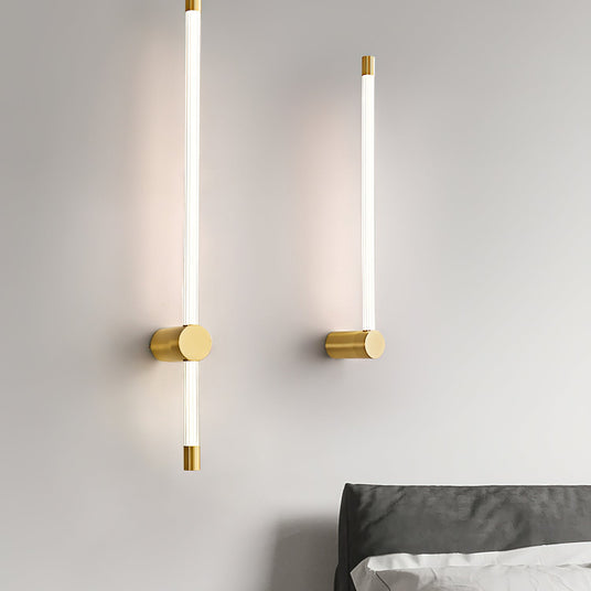 A lit pair on a bedroom wall beside a bed with dark bedding and a pale throw