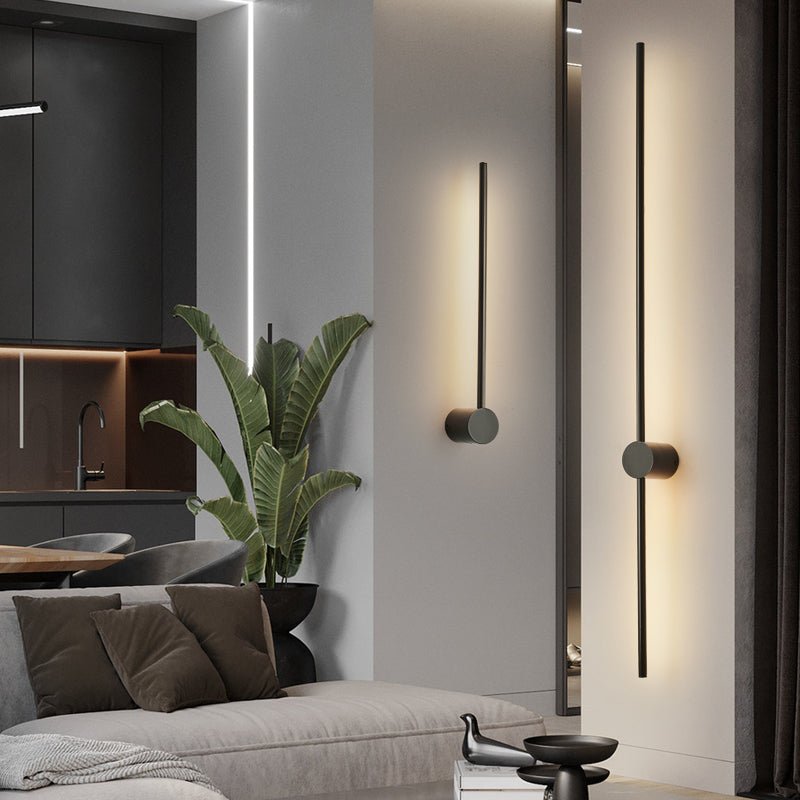 Two rods lit on a pale wall beside a tall plant and a dark sideboard
