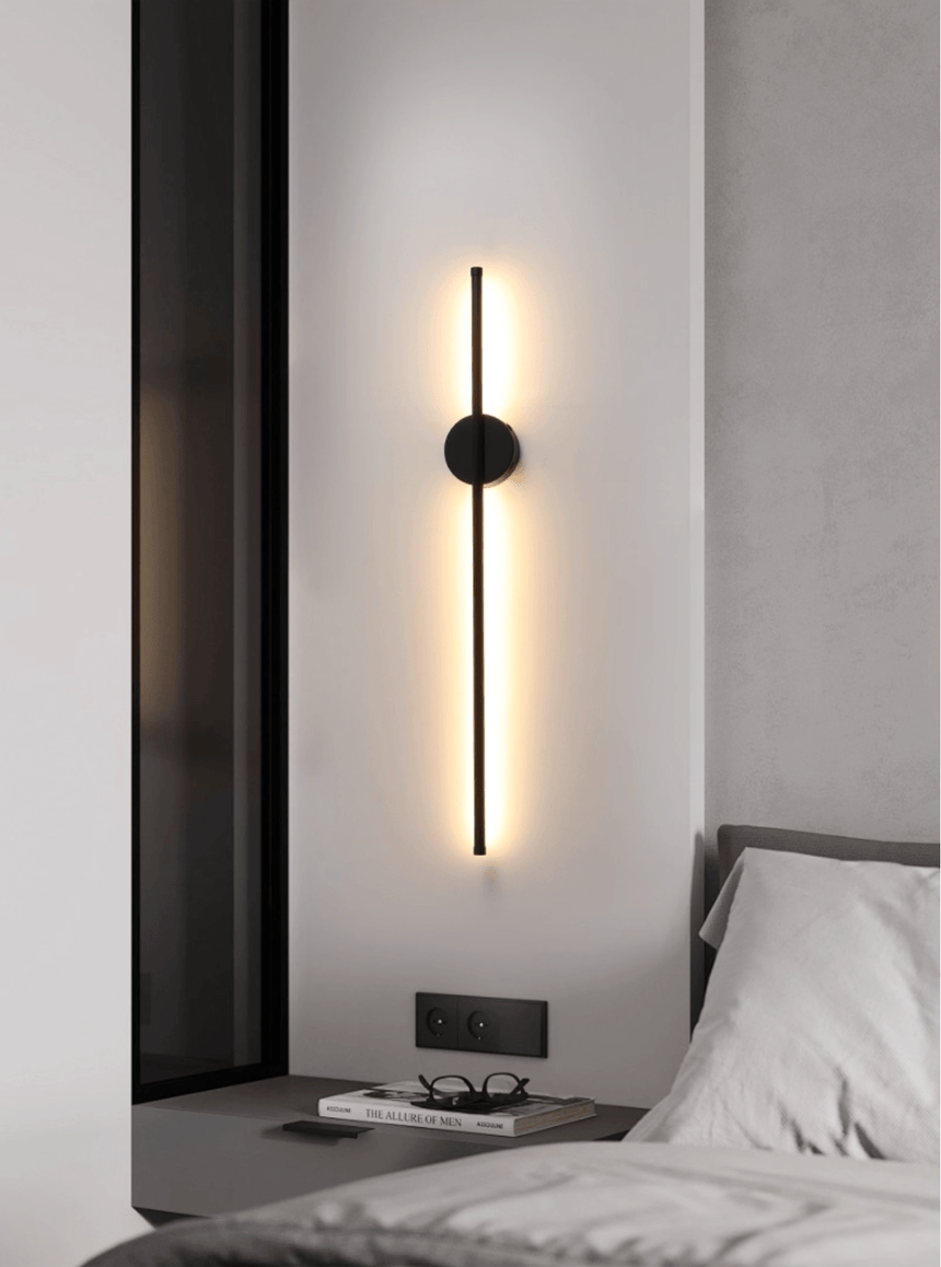 Mounted vertically beside a bed, the bar lit against a pale bedroom wall