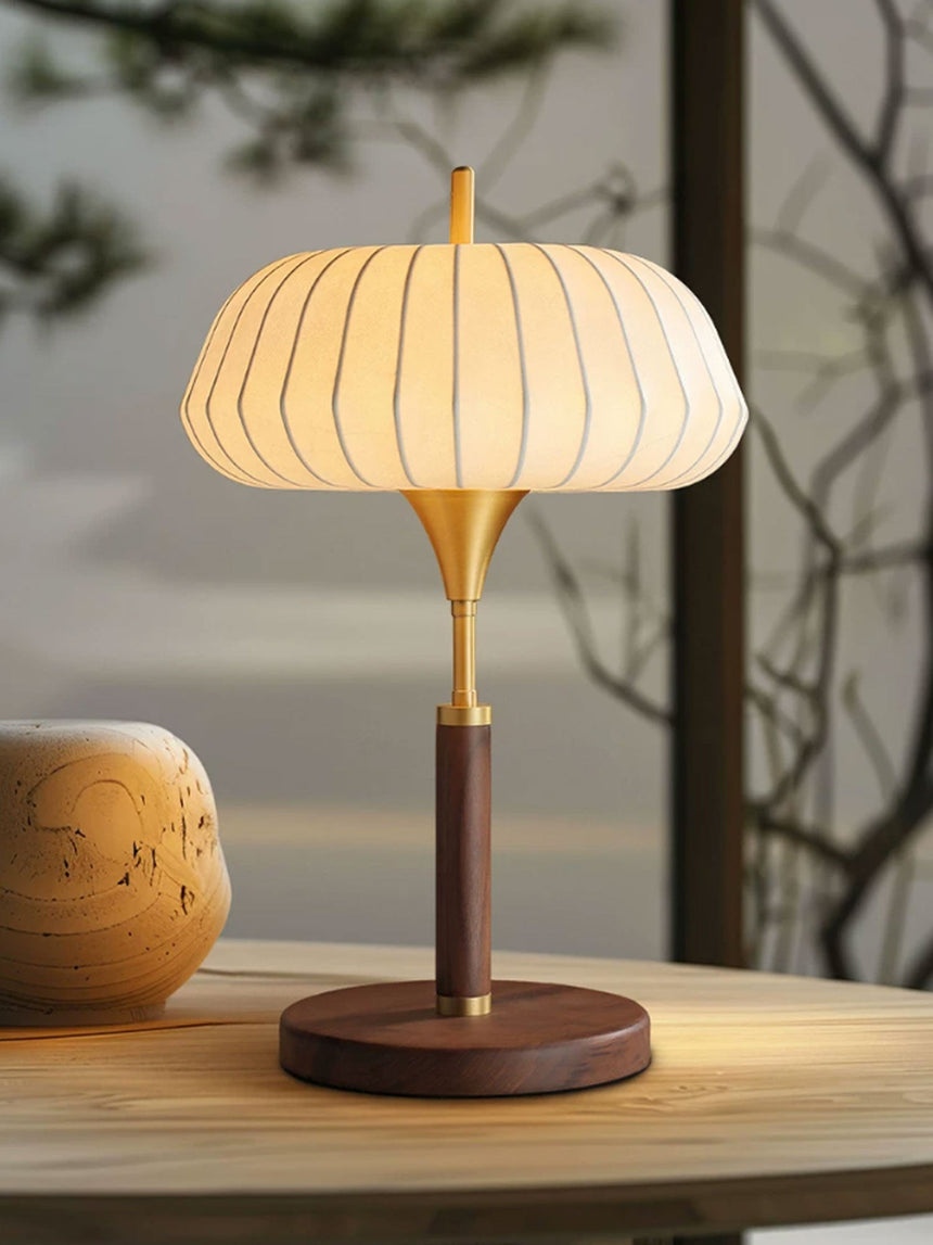 Remote control table lamp lit on a wooden table beside a pale vase