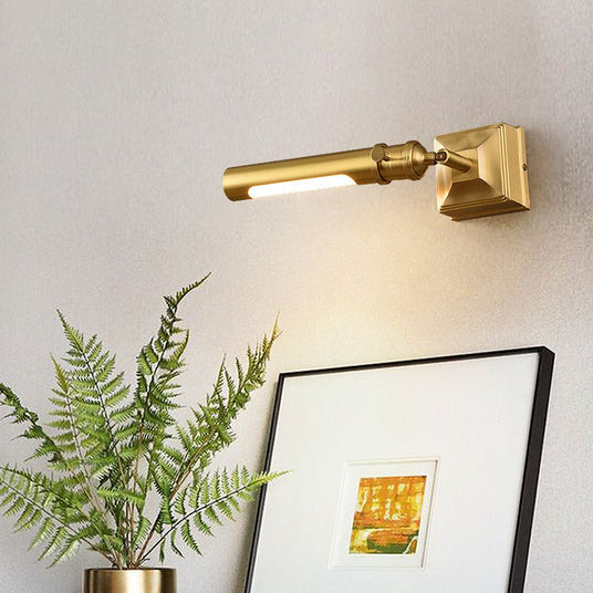 Brass tube lit above a framed artwork beside a fern in a brass planter
