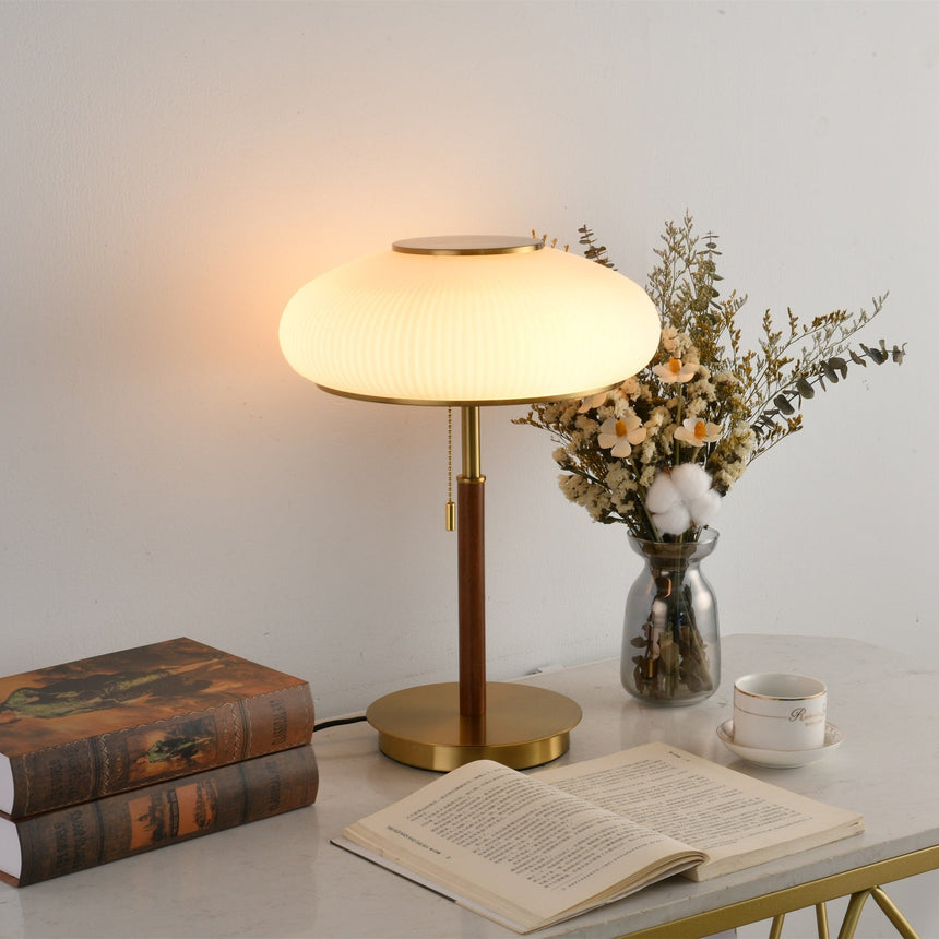 Ribbed glass table lamp lit close beside dried flowers and books