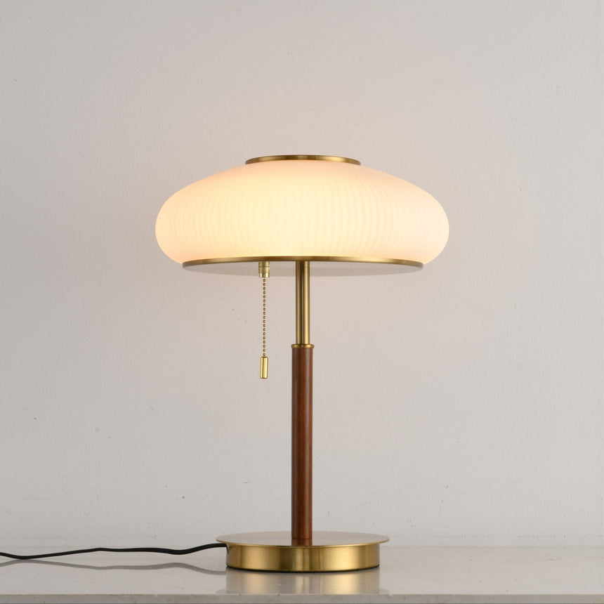 Ribbed glass table lamp lit against a plain pale ground