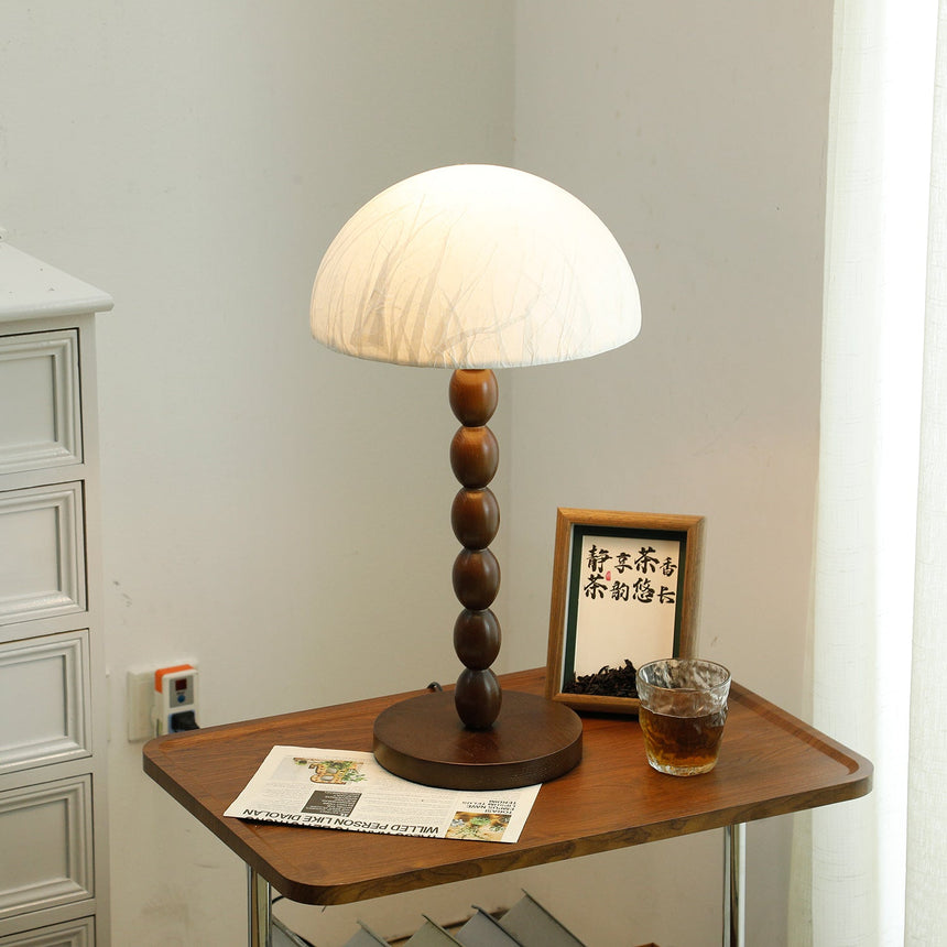 Rice paper table lamp lit on a table beside a glass of tea