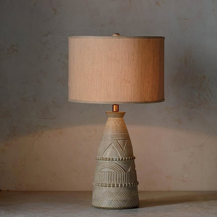Tapered carved base with chevron bands under a beige drum shade, unlit