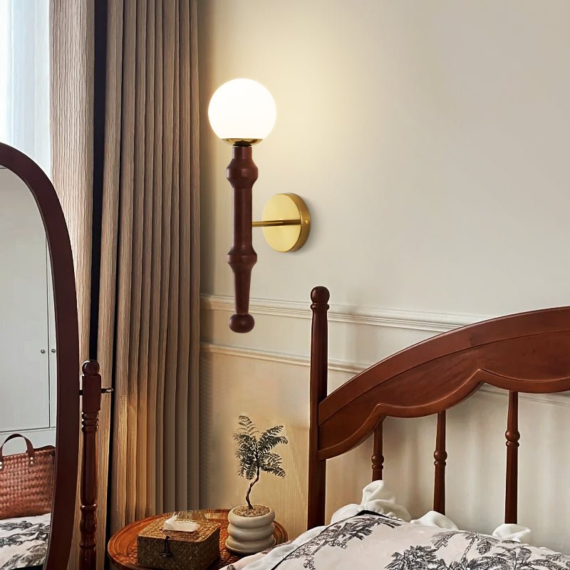 Sconce lit beside a spindle bed with a curtain and a small plant below