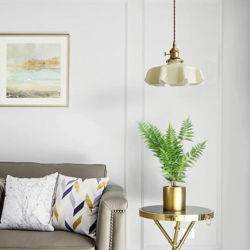 Beige scalloped shade over a gray sofa with a fern on a brass side table