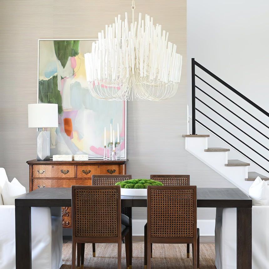 Chandelier lit above a dark dining table with cane back chairs