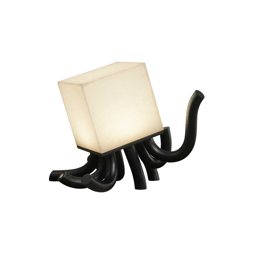 Sculptural table lamp in black seen at an angle, lit, plain ground