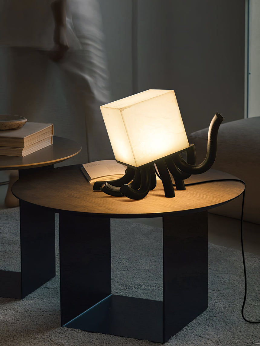 Sculptural table lamp lit on a black side table beside books