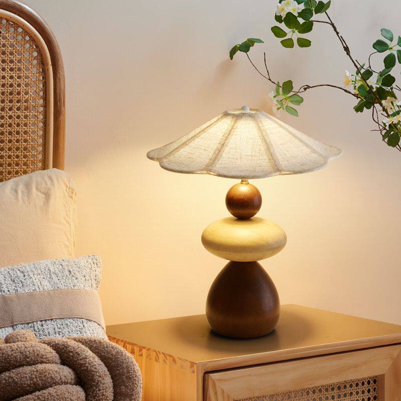 Sculptural table lamp lit on a nightstand beside knitted cushions