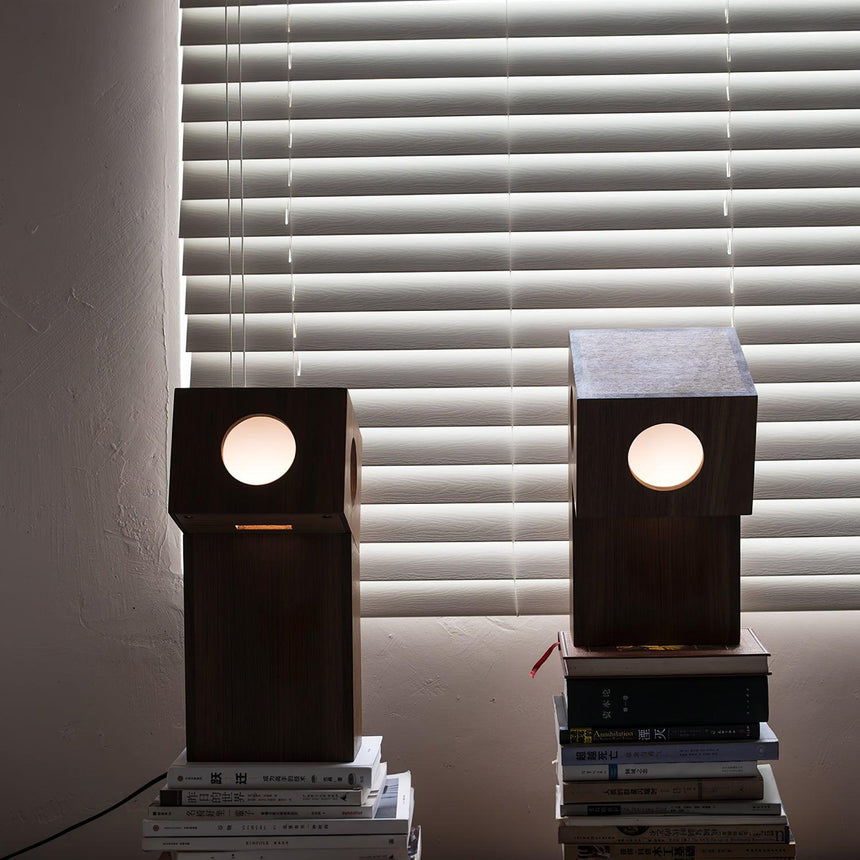 Two teak lamps lit on books in front of a window with blinds