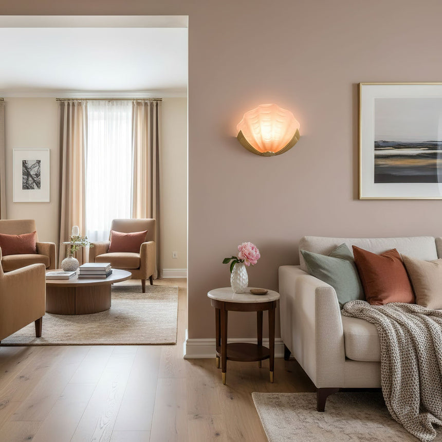 A shell sconce lit on a pink wall above a sofa, a side table and a rug