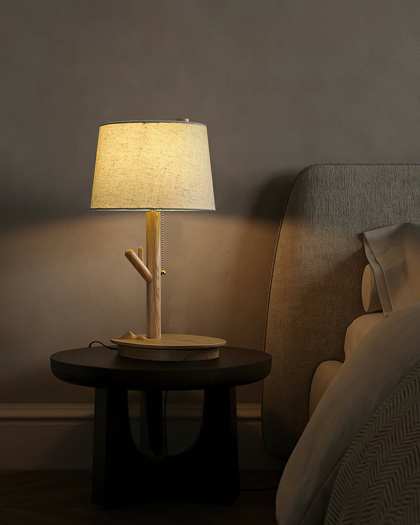 Branch stem lamp lit on a black side table beside a bed at night