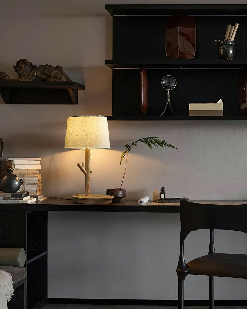 Branch stem lamp lit on a dark work desk below shelves of small objects