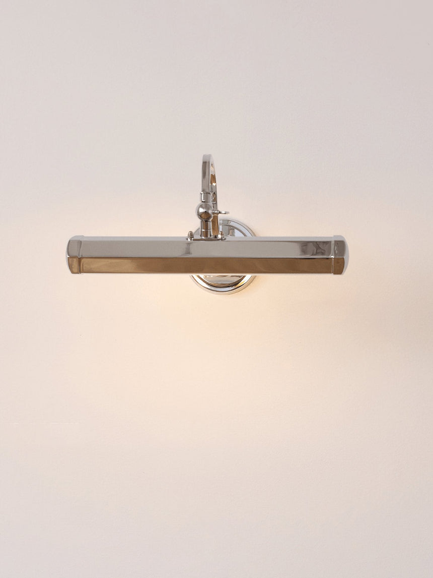 The chrome version lit on a pale wall, a hooded bar on a curved arm