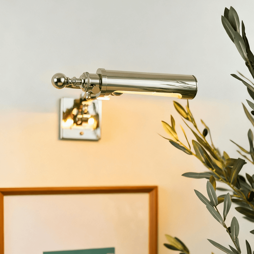 Polished tube lit over the top edge of a framed print with foliage nearby