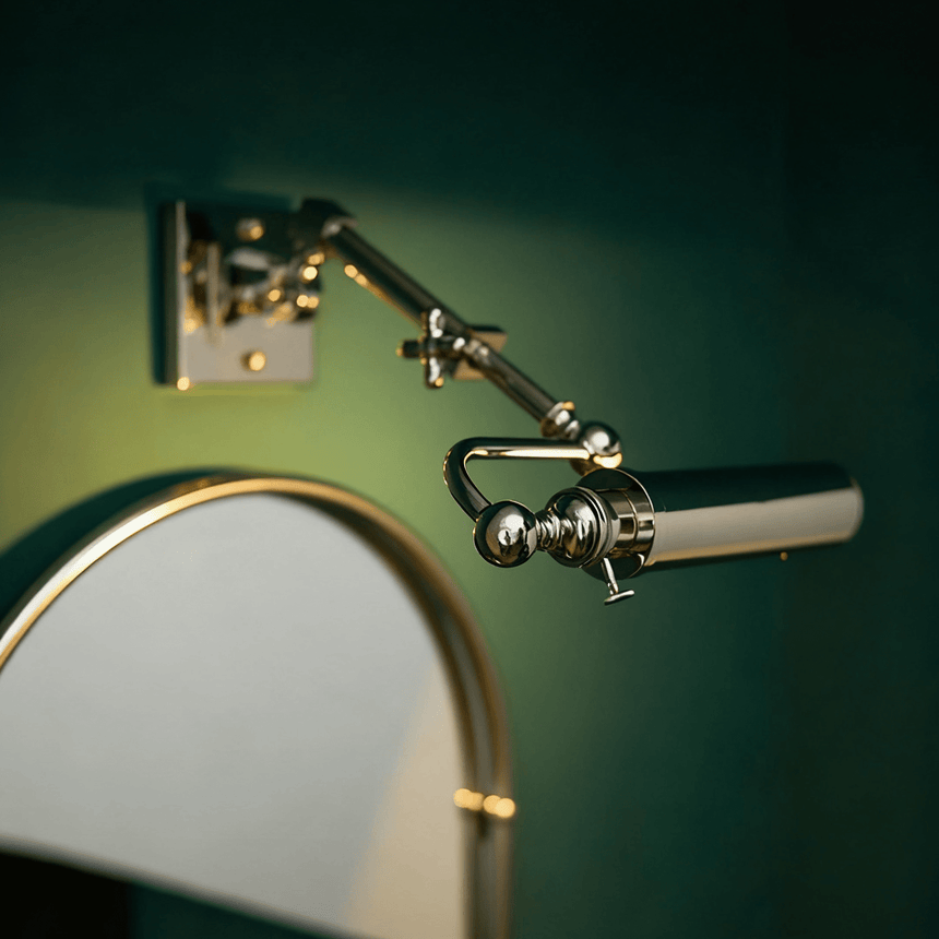 Polished tube lit beside an arched mirror on a deep green painted wall