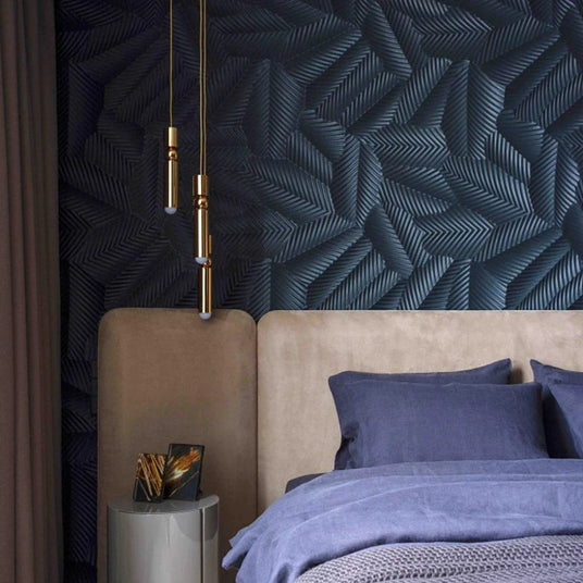 A slim gold tube pendant lit beside a bed with a padded headboard