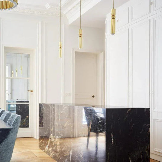 Two slim gold tube pendants lit in a bright hallway beside a doorway