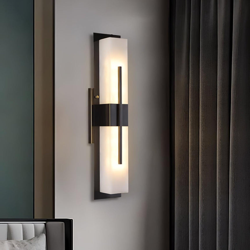 The sconce lit on a pale wall beside a dark green curtain and a chair