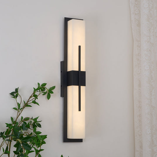 The sconce lit on a wall beside a linen curtain with leaves in front