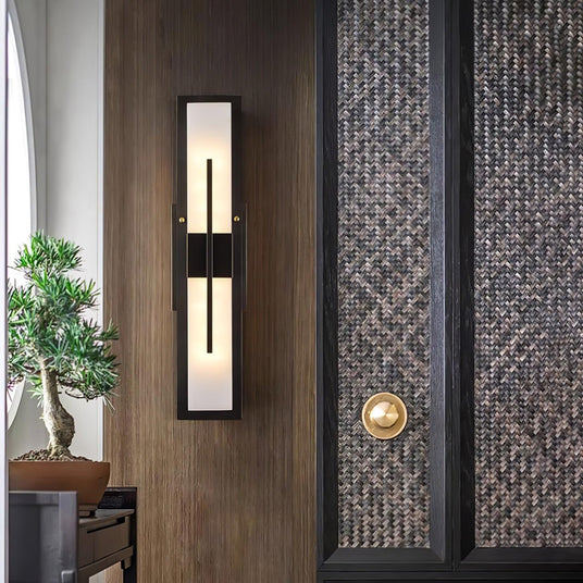 The sconce lit beside a timber entry door with a bonsai on a console