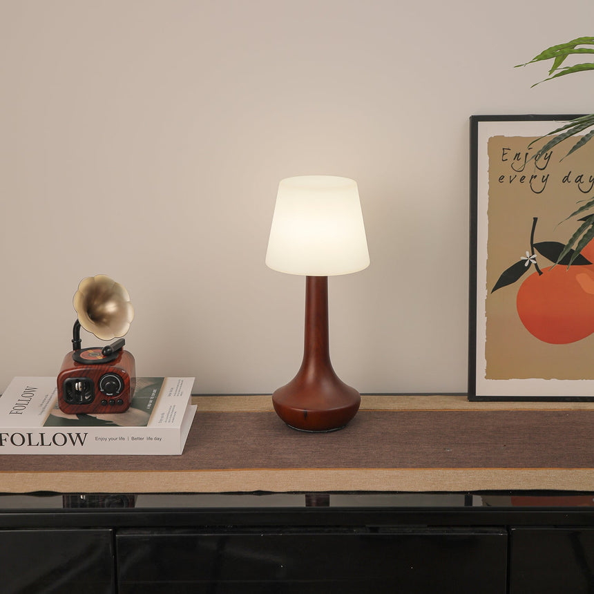 Small walnut lamp lit cool on a shelf beside a framed picture