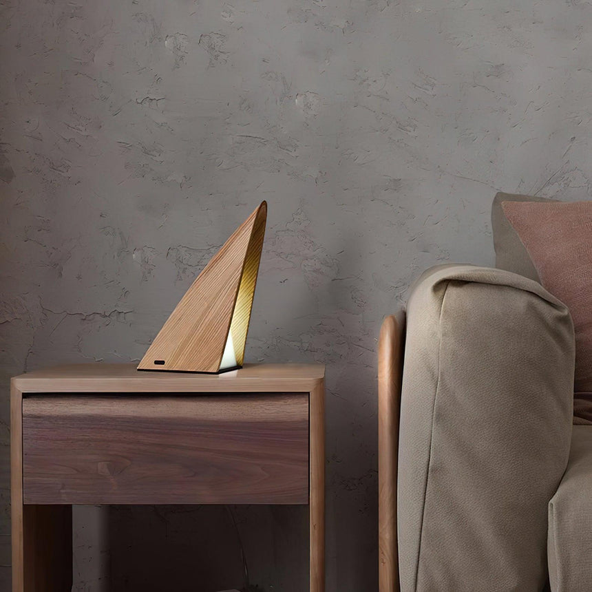 Small bedside lamp lit on a walnut nightstand beside a draped chair