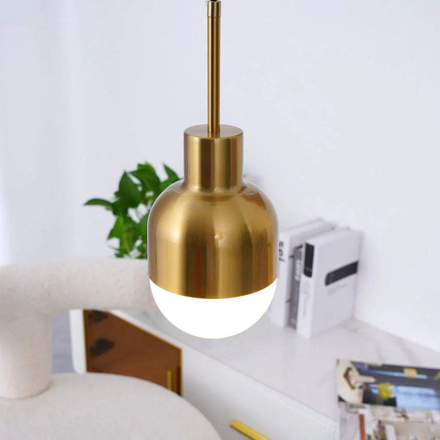 The brass pendant lit above a desk with a plant and framed pictures