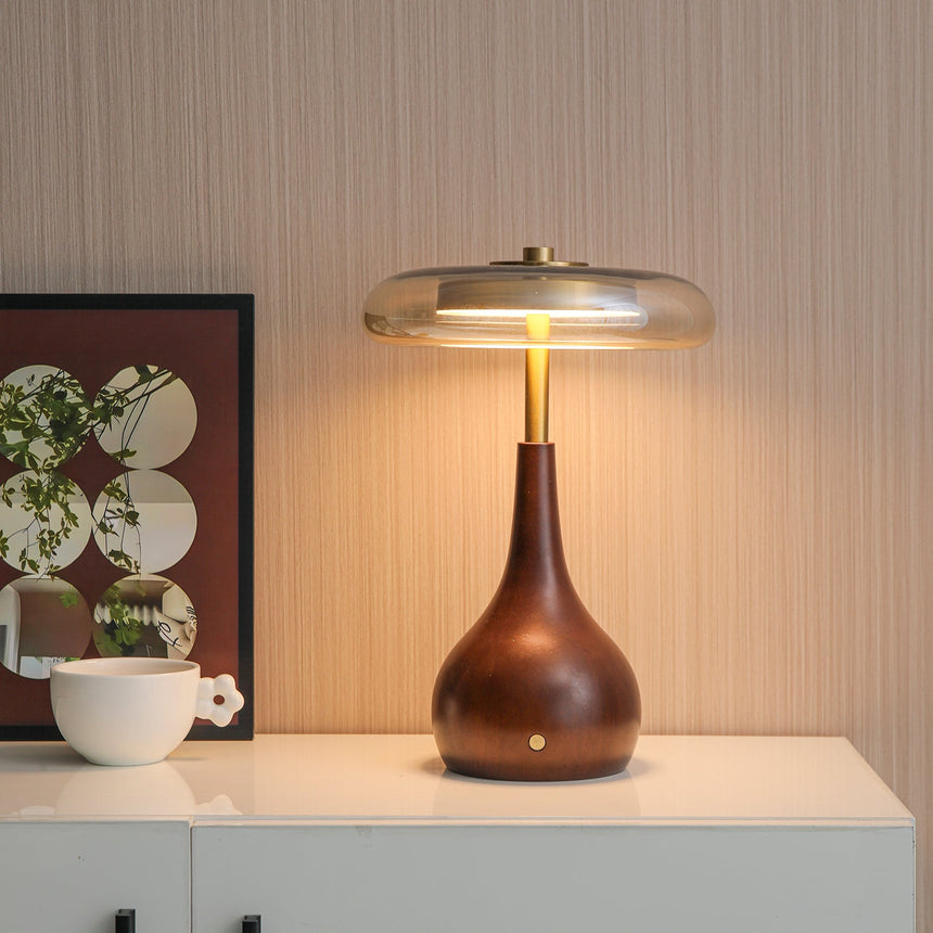 Small table lamp lit on a white cabinet beside a print and a cup