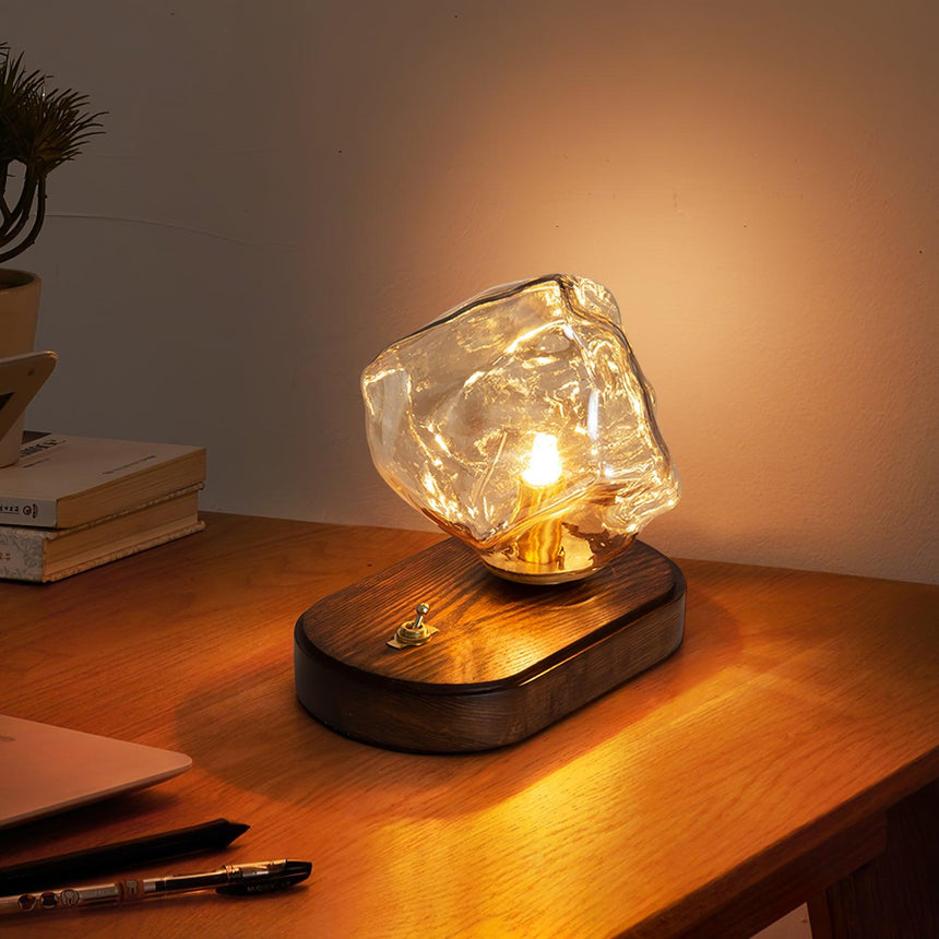Glass ice form lamp lit on a desk beside a pen and papers