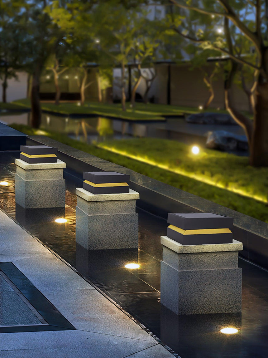 Caps lit along pillars beside a planted garden path at night