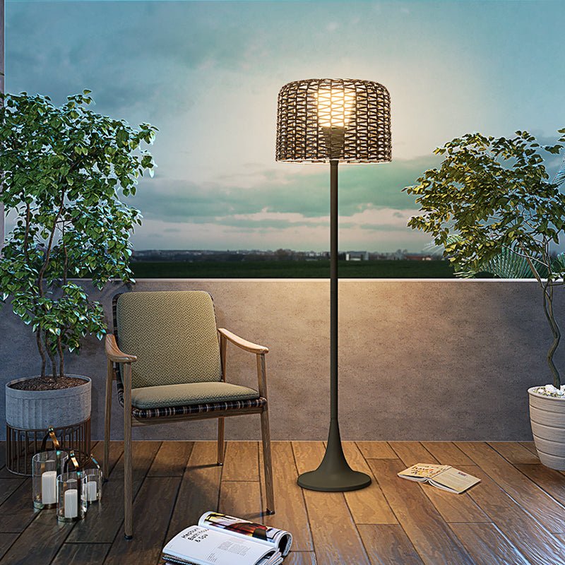 The lamp lit on a timber deck beside a wooden armchair and a potted tree