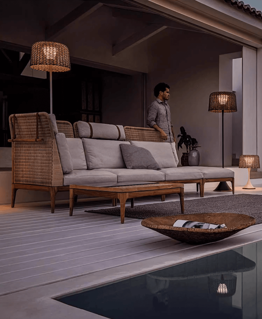 The lamp lit on a deck beside a pool with a long sofa and a low table