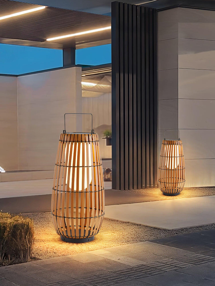 Two lanterns lit at a paved entrance beside a planted border at night