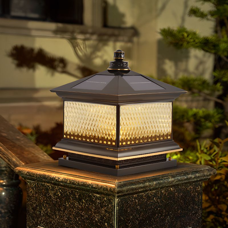 The lantern lit on a pillar with a house and planting behind it at dusk