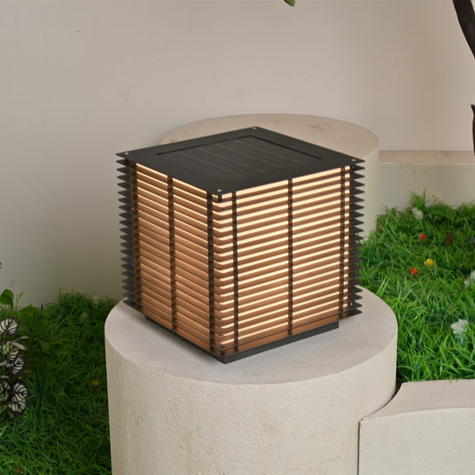 The cube lit warm on a pale stone plinth with grass and a tree behind it