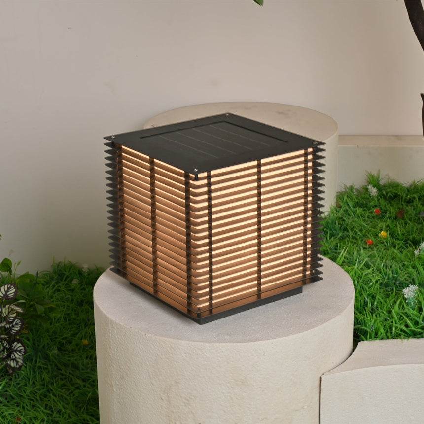 The cube lit warm on a pale stone plinth with grass and a tree behind it