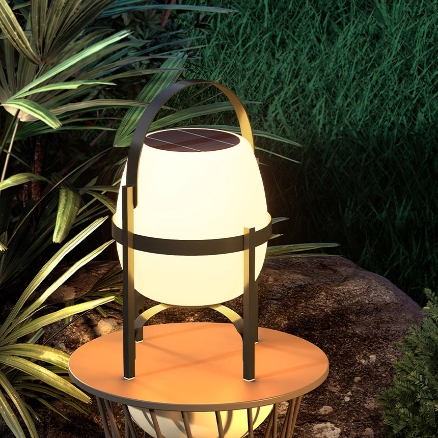 The lamp lit on a round wood table with tall planting behind it at night