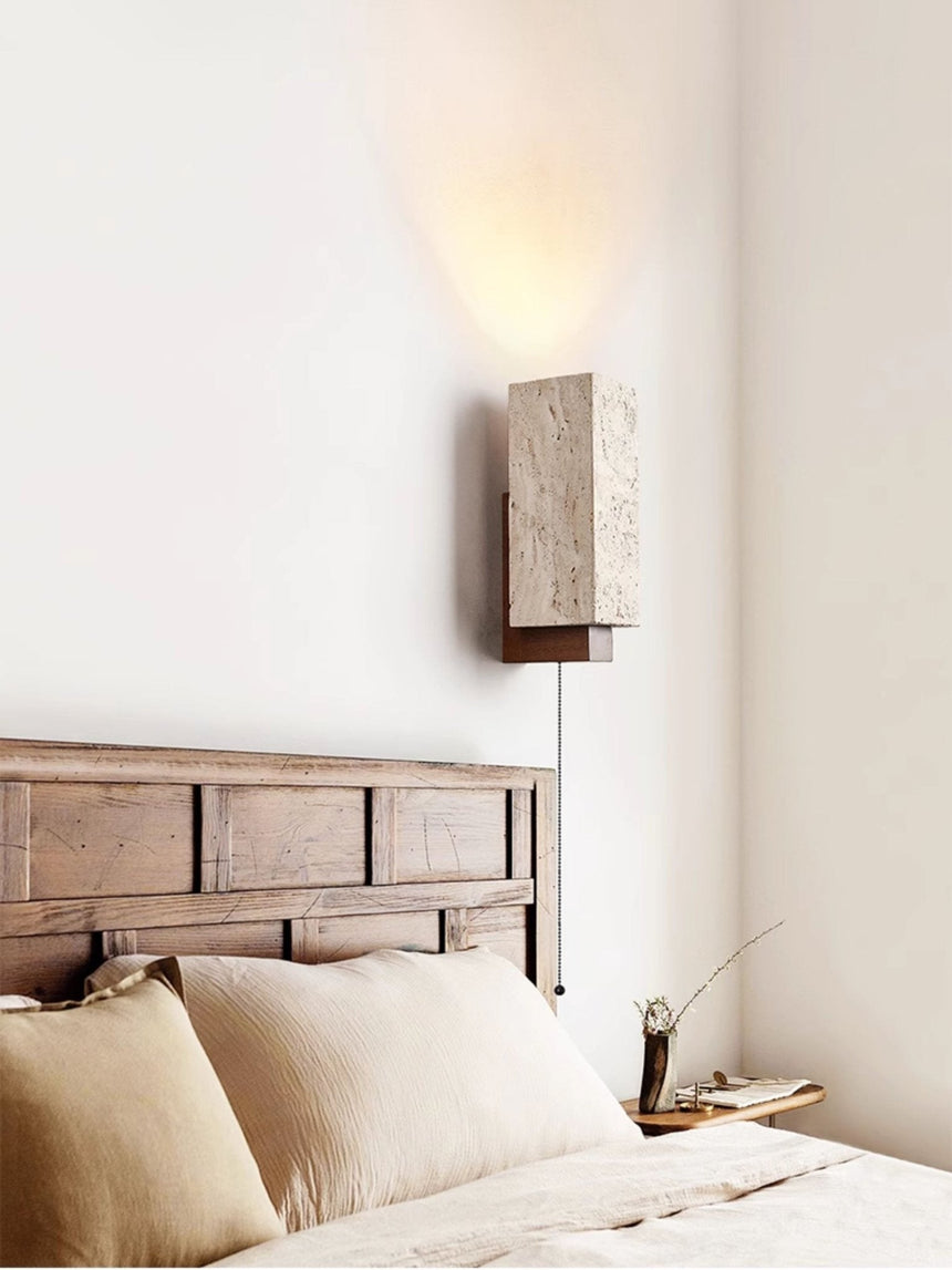 Sconce lit beside a wood headboard above a bed with linen pillows