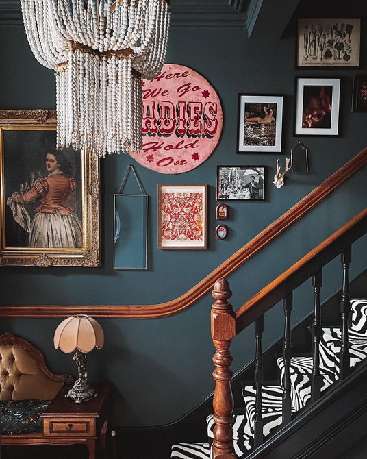 Hung in a stairwell above a gallery wall of framed pictures and a banister