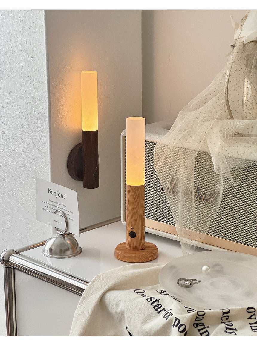 Two lamps lit on a shelf beside a mirror and a fold of white linen fabric