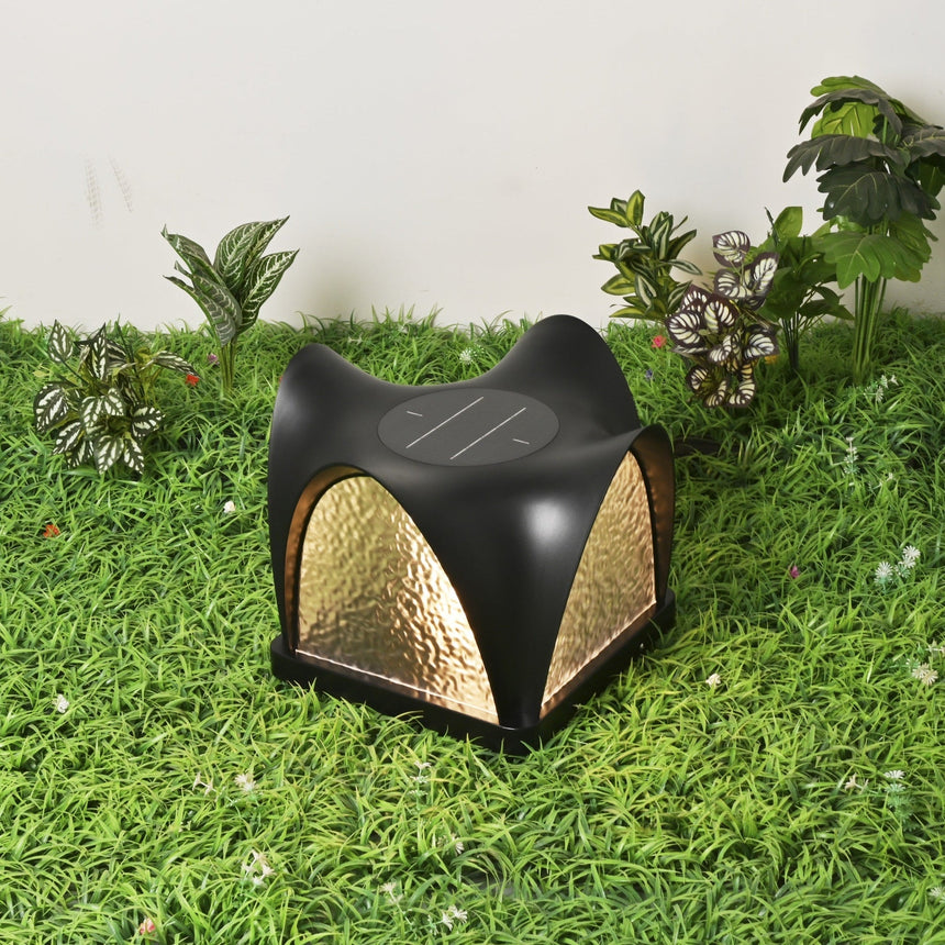 The petal cap lit on a lawn beside low planting after sunset