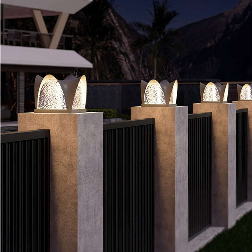 Petal caps glowing on pillars above a slatted fence in the evening