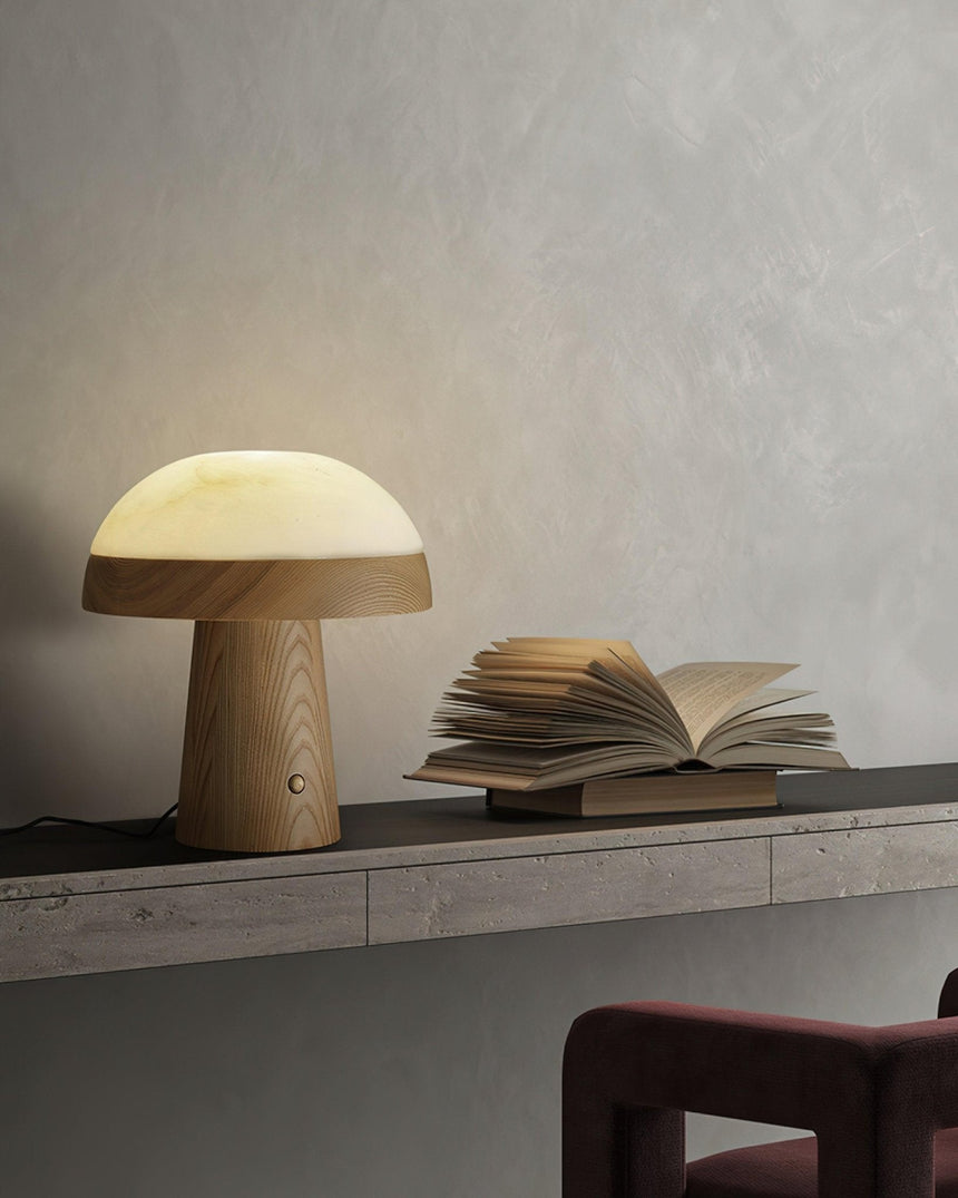 Stone table lamp lit on a long shelf beside an open book
