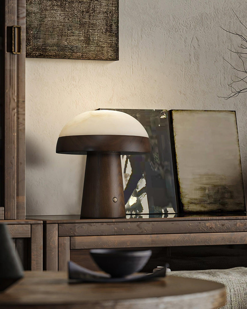 Stone table lamp lit on a console beside leaning framed art