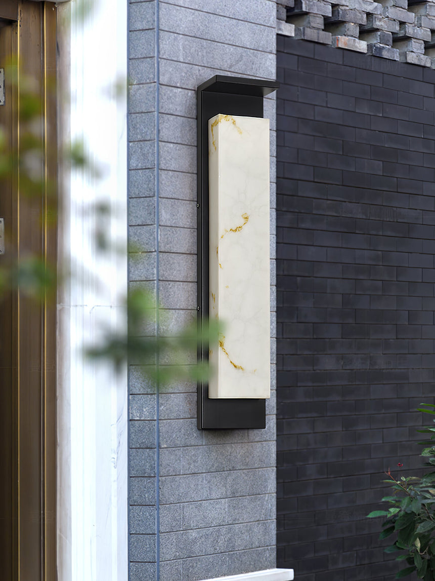 The light on a gray brick corner with leaves crossing the foreground